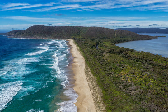 Aerial scene capturing Seven Mile Beach and Wallis Lake near Forster, NSW, Australia, separated by a narrow strip of coastal land and leading towards Booti Hill. 