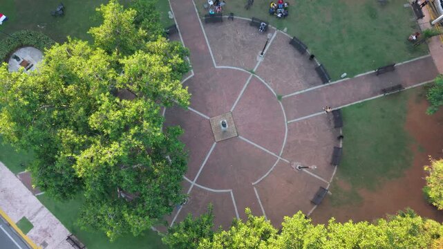 High-angle aerial drone shot capturing a top-down perspective of the circular architecture and green spaces of Rub&eacute;n Dar&iacute;o Plaza, featuring surrounding urban streets, pedestrians, and traffic in Santo