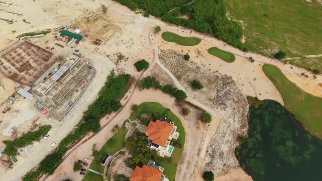 Aerial drone footage capturing a high-angle view of luxury villas, golf course fairways, and ongoing resort construction in Punta Cana, Dominican Republic. The shot transitions from a close-up of resi