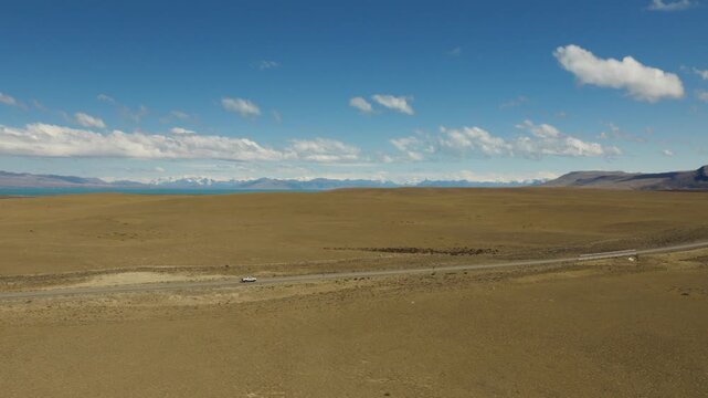 Pickup truck travels across Patagonian steppe on Ruta Nacional 40 in Santa Cruz, Patagonia, Argentina, with Southern Patagonian Andes visible on the horizon, wide panoramic drone tracking shot.