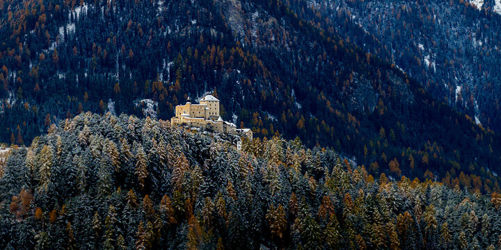 Aerial view of Schloss Tarasp perched on a forested hill with autumn colors and light snow in Scuol, Graubunden, Switzerland.
