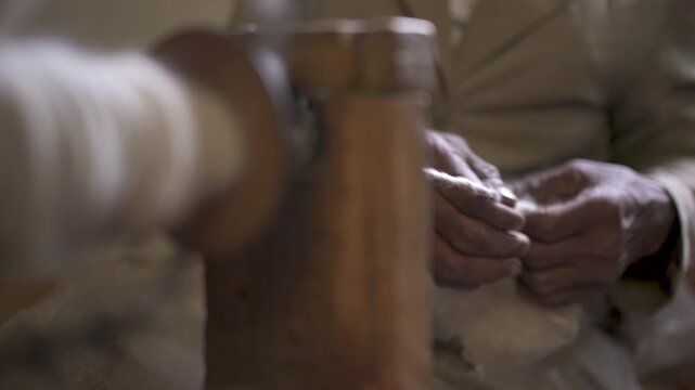 A manually operated spinning wheel turns as wool fibers are carefully spun by hand into woolen yarn. Perfect for historical and agricultural documentary.