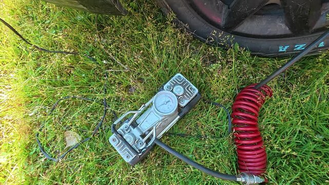 A portable tire inflator with a pressure gauge and red coiled hose sits on green grass next to a car tire