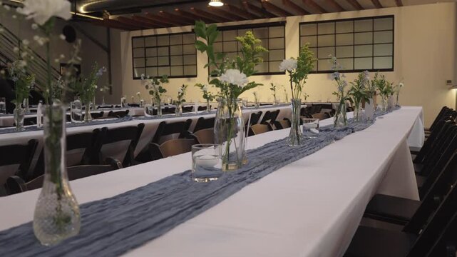 Rows of tables adorned with delicate floral vases and blue runners in a stylish event space.