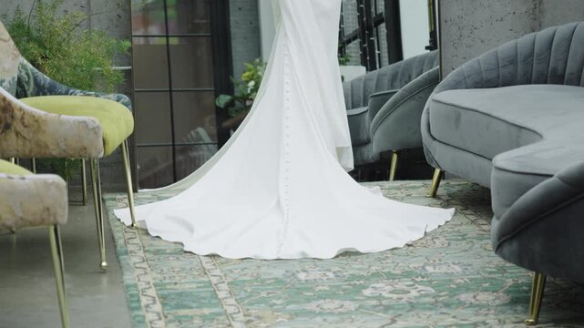 A bridal gown's train elegantly drapes over a patterned carpet, surrounded by plush seating in a contemporary lounge. Ideal for wedding fashion or interior design themes.