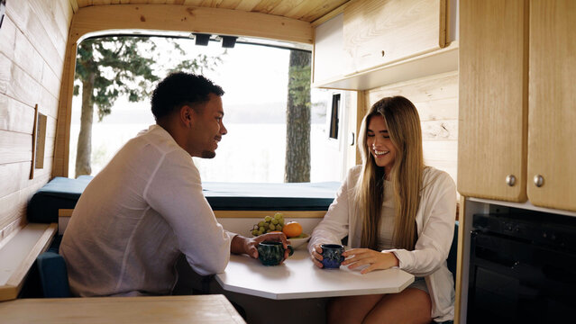 Happy couple enjoying a conversation and coffee inside a cozy camper van, embracing the freedom of van life travel