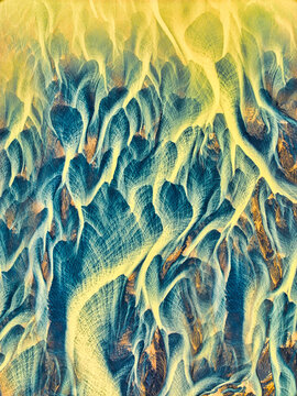 Aerial view of abstract patterns of a glacial river delta with golden sediment and blue water flowing through intricate channels in Hella, Rangarthing ytra, Iceland.