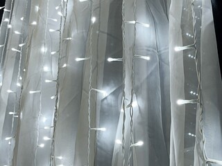 Naklejka premium A string of white LED lights arranged in vertical strands, elegantly draped over translucent white tulle fabric, creating a soft, glowing effect
