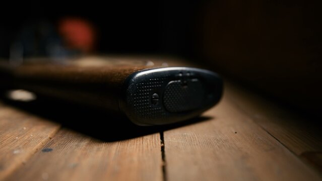 The checkered buttplate of a vintage military rifle stock rests on a rustic wooden table surface in this low angle shot emphasizing the textured grip and aged material of the classic firearm.
