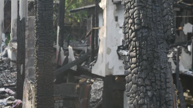 Fire disaster aftermath exterior view of burned destroyed residential house with charred wooden columns collapsed structure and debris