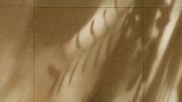 Soft abstract shadow of tropical plant leaves and branch cast on warm beige golden tile floor surface in morning sunlight indoor background