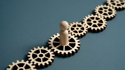 Wooden human figure stands on a gear in a line of gears, representing teamwork and process. © Palash Art