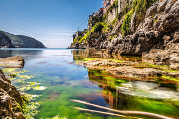 Fototapeta premium Clear Turquoise Sea Water with Mossy Rocks and Ancient Historic Fortress Town Wall of Amasra