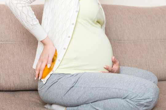 Pregnant woman suffer from back pain holds a hot bottle or warmer against her back. Concept pregnant woman lifestyle and health care