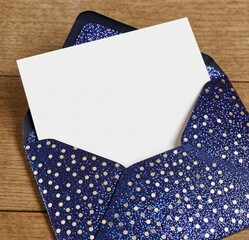 Obraz premium Blue Glitter Envelope with White Card on Wooden Surface for Invitations
