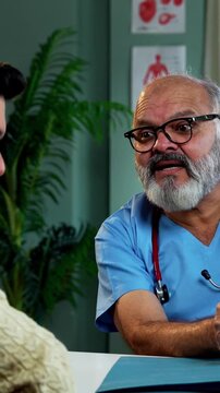 Indian male doctor using laptop while consulting young man patient as experienced physician discusses medical reports in modern Indian clinic OPD healthcare consultation