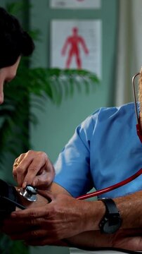 Indian male doctor checcking BP of young patient during routine health examination as experienced physician measures blood pressure inside modern Indian clinic OPD healthcare visit