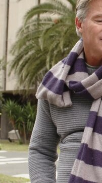 Vertical video: Camera filming mature man turning head smiling at curb in striped scarf, copy space