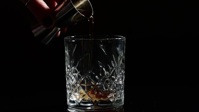 Bartender hand pouring syrup into empty glass for cocktail preparation, first step of mixing drink, slow precise movement, thick sweet liquid falling into tumbler, black background, professional 