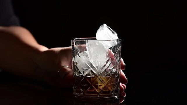 Ice cubes falling into cocktail glass in slow motion on black background, frozen blocks dropping into liquid, splash and bubbles rising, dramatic detailed shot, cold refreshing drink preparation, prof