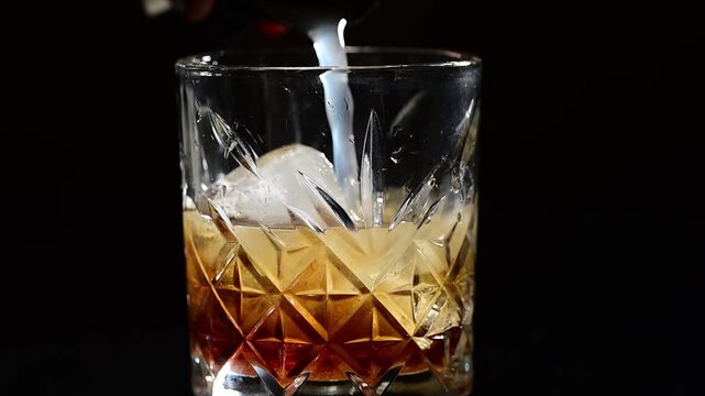 Slow motion pouring of sweet syrup into cocktail glass during preparation, thick liquid stream falling into drink, black background, professional bartending process, cocktail making tutorial, stylish 