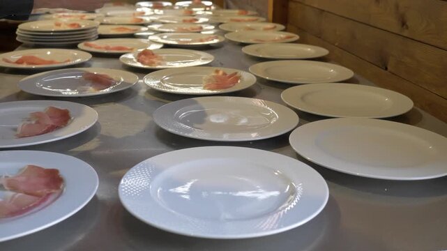 Restaurant staff carefully place prosciutto slices onto appetizer plates while preparing dozens of starters for a large celebration and banquet service.