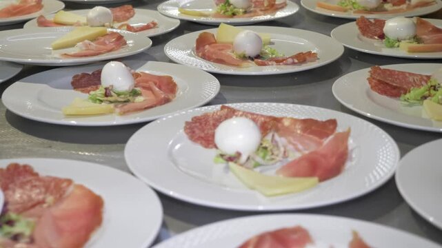 Restaurant staff complete appetizer plates with prosciutto, salami, mozzarella, cheese and fresh salad before service begins.