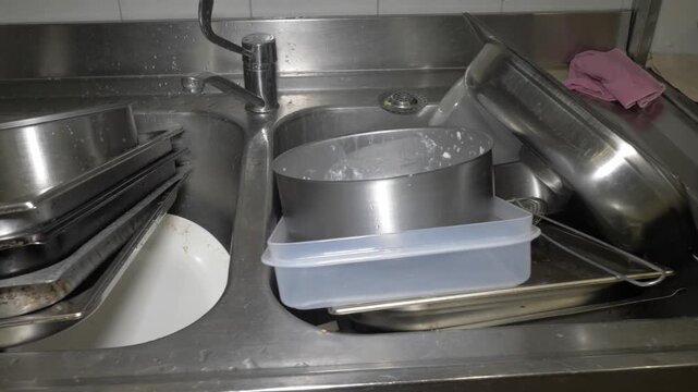 A pile of dirty pots and dishes sit in the restaurant kitchen sink, waiting to be washed after a busy catering event, capturing the unglamorous reality behind every great meal.