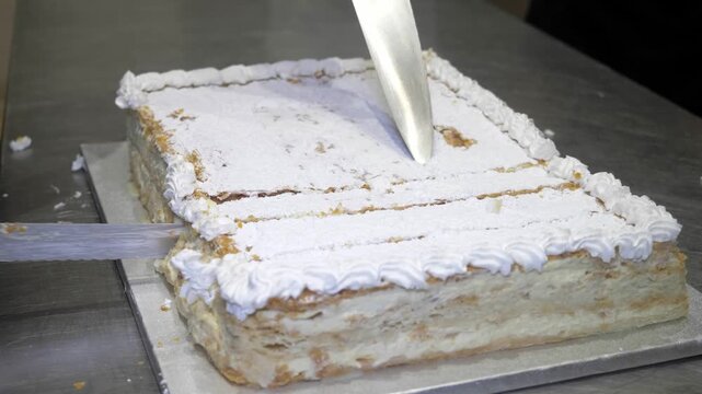 A chef carefully cuts the celebration cake into neat small portions, preparing to serve a sweet finishing touch to guests at the end of the lively catered party event.