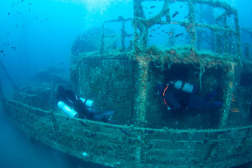 Naklejka premium Scuba diving at shipwreck site with divers exploring underwater shipwreck in clear water