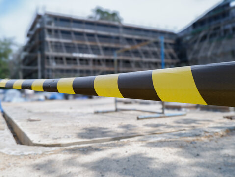 ​Yellow and black caution tape close up with blurred building construction site background, safety warning tape at industrial development area