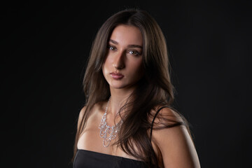 Naklejka premium Female model wearing elegant diamond necklace with long hair posing in studio against black background