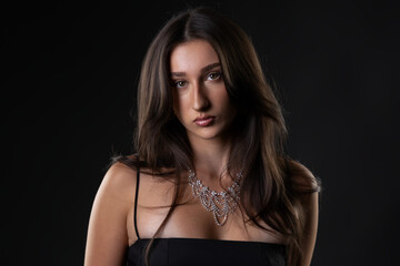 Naklejka premium Female model wearing a black dress and sparkling necklace on a dark background