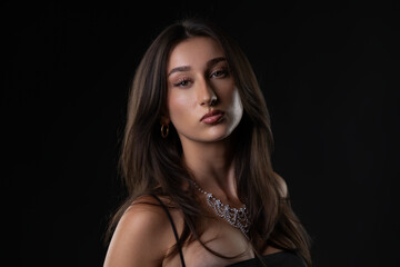 Fototapeta premium Female model wearing elegant jewelry and makeup looking at camera on dark background