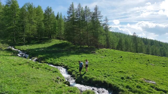Couple crossing a mountain stream immersed in a lush green landscape