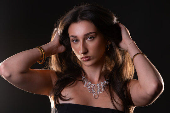 Female model posing with hands in hair, wearing necklace and bracelets, against a black background