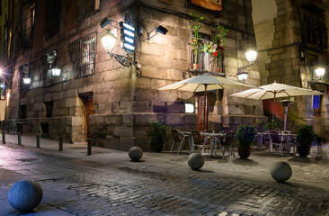 Obraz premium Cozy old street with table of restaurant in Madrid, Spain. Architecture and landmark of Madrid. Night cityscape of Madrid.