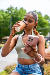 Obraz premium Young woman multitasking, drinking coffee and using smartphone outdoors