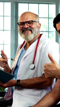 Indian male doctor with young male patient smiling showing ok sign after successful treatment as experienced physician gives thumbs up inside modern Indian clinic OPD healthcare visit
