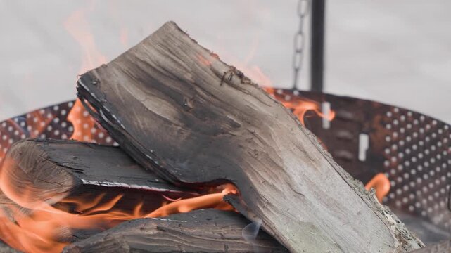 firewood burning in outdoor fire pit close up with bright flames and stacked wooden logs