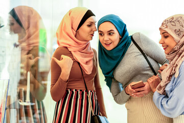 Obraz premium Three women in hijabs smiling and shopping together indoors.