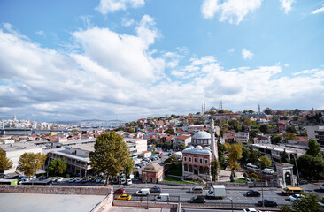 Obraz premium Wide elevated view of Istanbul with mosque domes, minarets, busy roads, trees and bright clouds across the historic skyline.