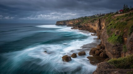 Obraz premium A dramatic coastal cliff under moody skies with waves crashing against rocks, showcasing the raw power of the sea and rugged natural beauty.