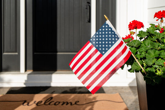 American Flag and Welcome Doormat at Front Door of House with Red Geraniums