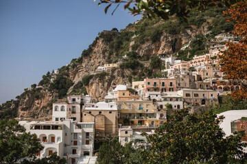 Obraz premium Scenic vista of Positano's pastel-colored houses clustered beneath a towering, rocky mountain cliff.