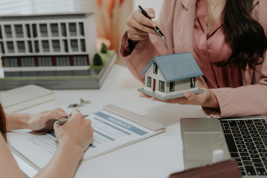 Real estate agent explaining insurance policy to client, holding house model in office.