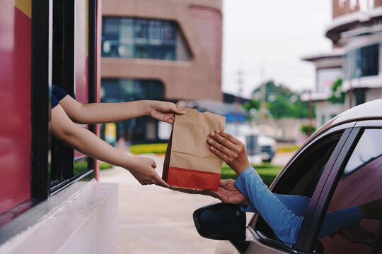 A customer picks up a French fries burger from a drive-thru counter employee during rush hour.