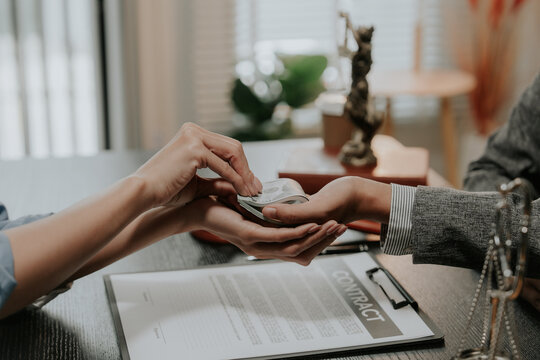 Close-up of person giving bribe money in US dollars to a judge or lawyer at desk.