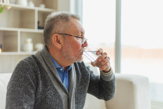 Senior man holding glass drinking fresh water at home. Mature old senior thirsty grandfather takes care of his health. Healthcare water balance. Elderly healthy lifestyle