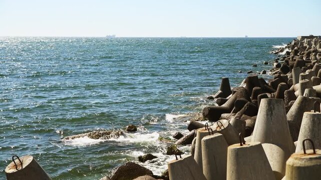 Sea waves crashing against coastal concrete wave breakers under bright sunlight